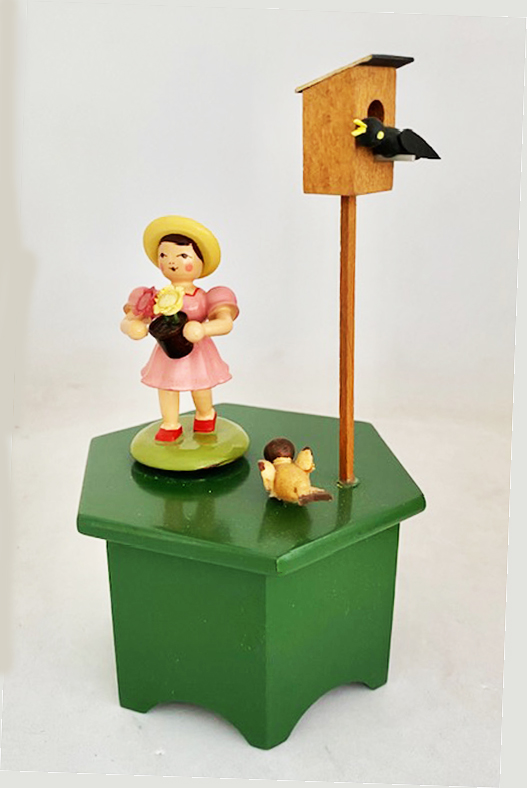 Revolving little girl holding flower pot near birds ad bird house on green platform